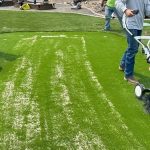 two person mowing artificial grass yard